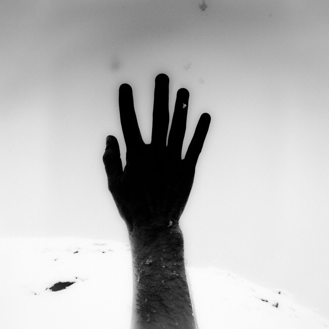 Monochrome image of an arm extending upward with an open hand against a muted background, creating a stark contrast in tones.
