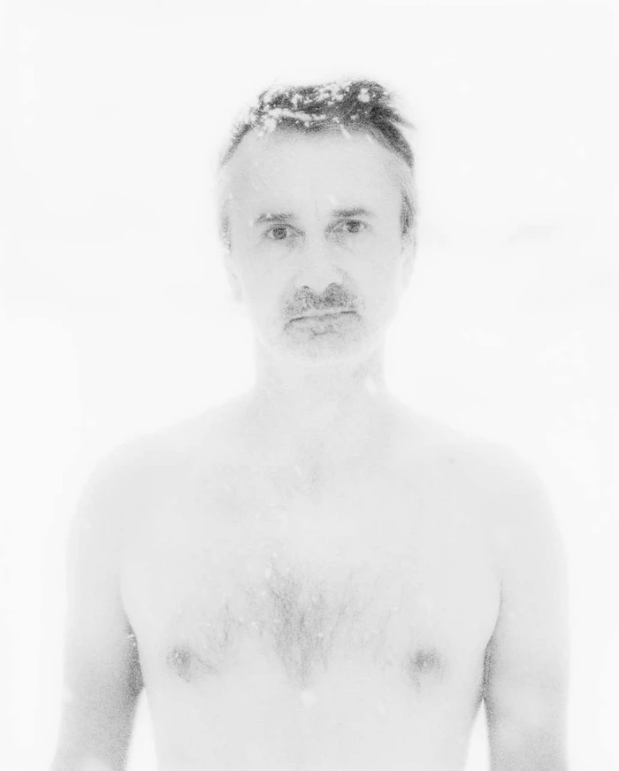 Portrait of a shirtless man with short hair and a mustache against a bright white background