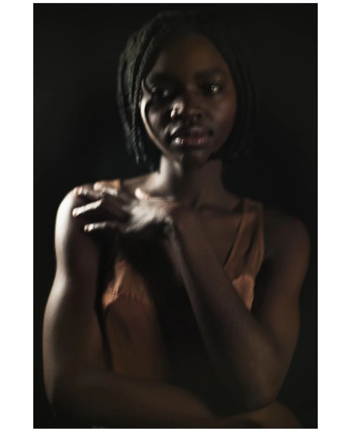 Low-key portrait of a black woman with braided hair touching her shoulder against a dark background
