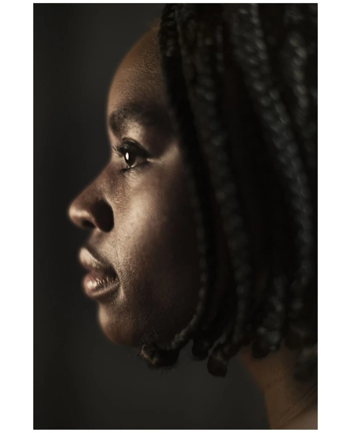 Close-up profile portrait of a black woman with braided hair captured in moody, low-key lighting.