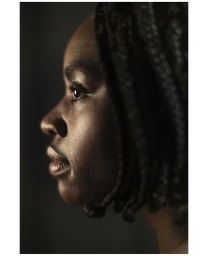Close-up profile portrait of a black woman with braided hair captured in moody, low-key lighting.