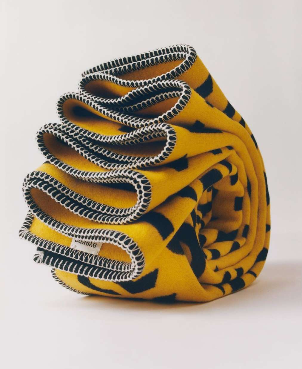 Folded yellow fabric with black geometric pattern and white stitching on a white background. Perfect for cozy comfort.
