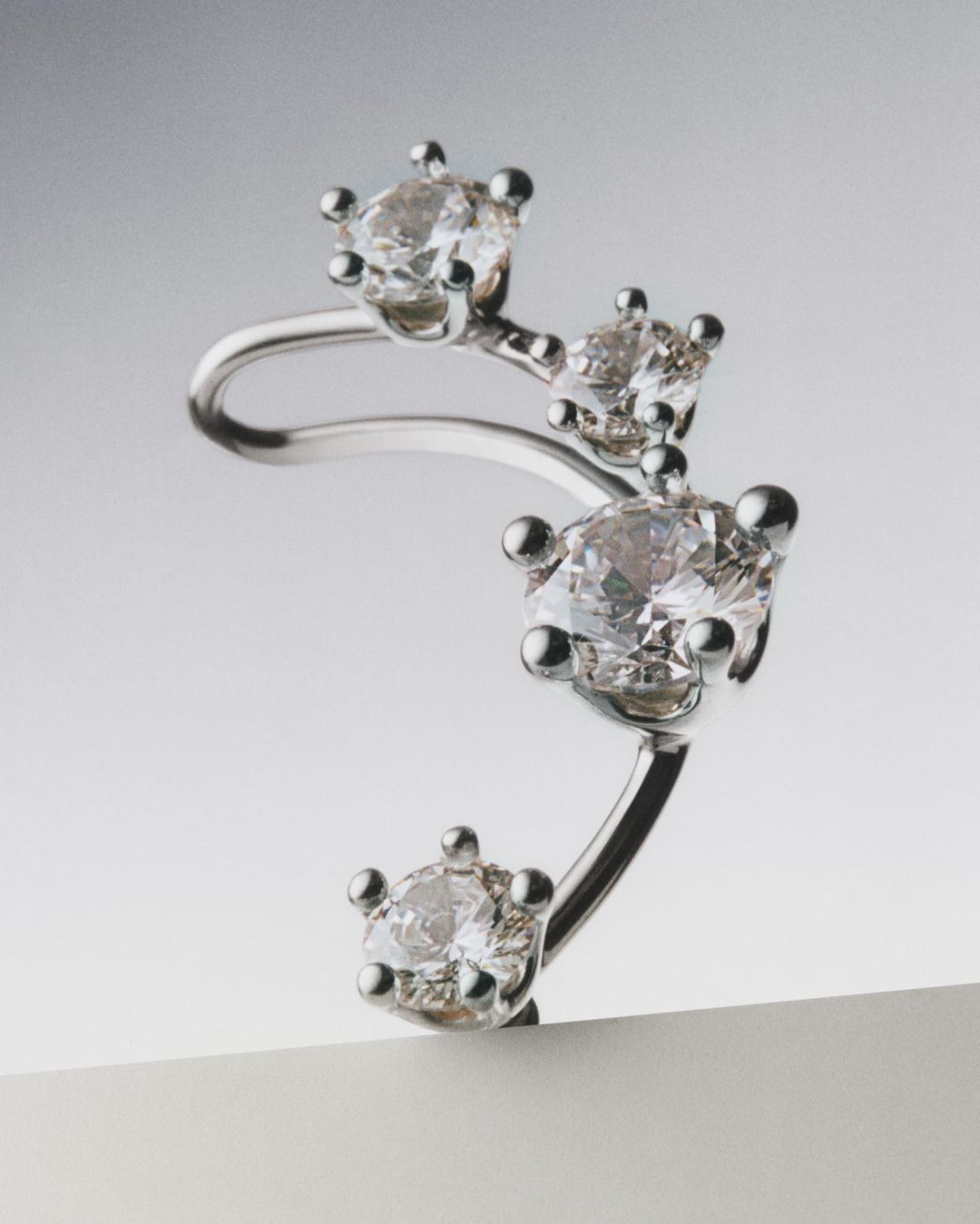Close-up shot of a silver ear cuff earring featuring four round-cut diamonds against a gradient gray studio background.