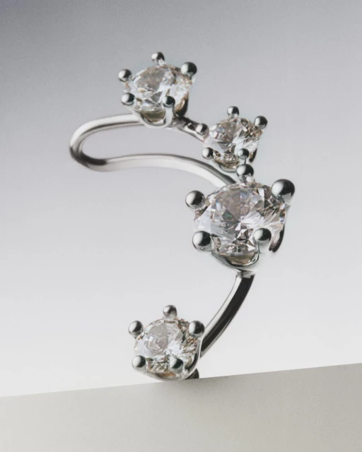 Close-up shot of a silver ear cuff earring featuring four round-cut diamonds against a gradient gray studio background.