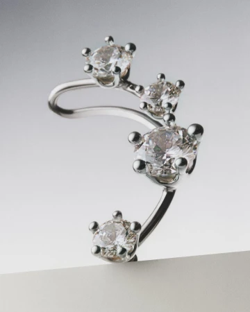 Close-up shot of a silver ear cuff earring featuring four round-cut diamonds against a gradient gray studio background.