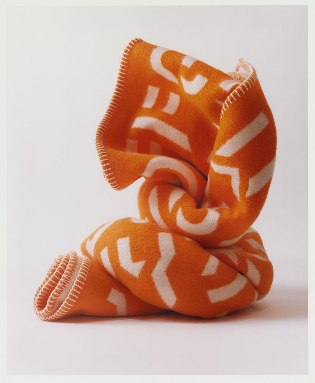Knotted orange blanket with white geometric pattern isolated on a white background. Soft, folded textile with decorative stitching.
