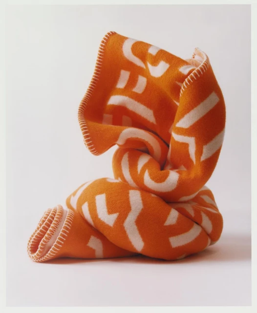 Knotted orange blanket with white geometric pattern isolated on a white background. Soft, folded textile with decorative stitching.