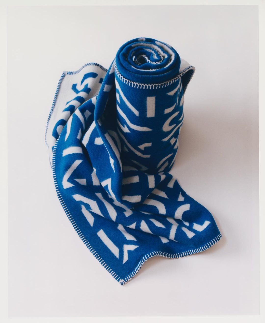 Blue and white blanket with geometric pattern, partially unrolled and stacked, showcased against a clean, light-colored background.