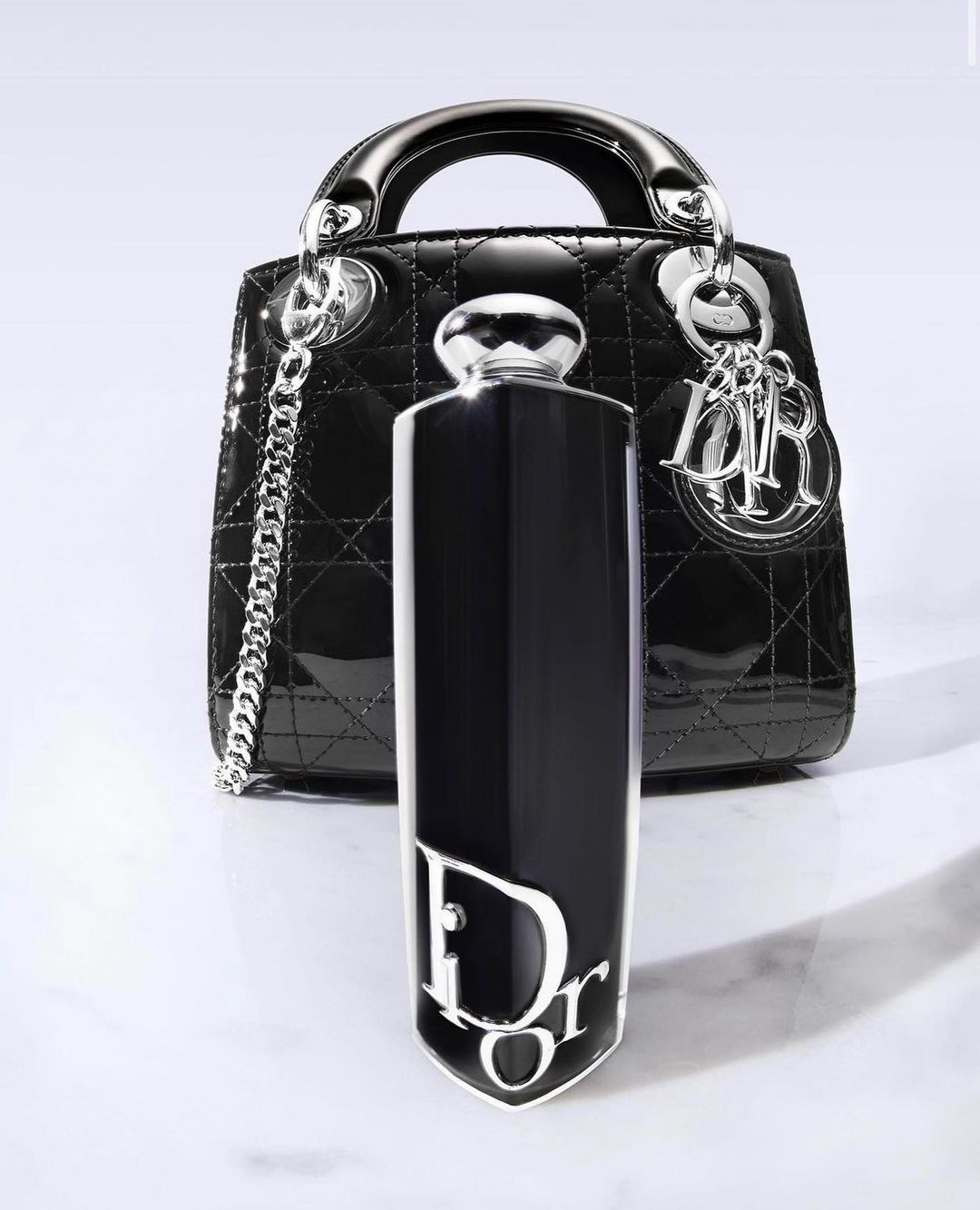Elegant composition featuring a black Lady Dior handbag and a Dior perfume bottle, set against a clean, bright background. 