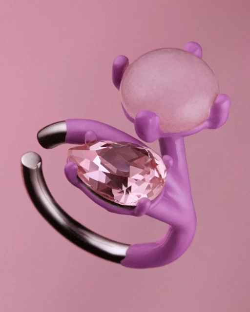 Still life featuring a pear-cut gemstone, a lavender abstract hand sculpture, and a frosted spherical object on a pink backdrop.
