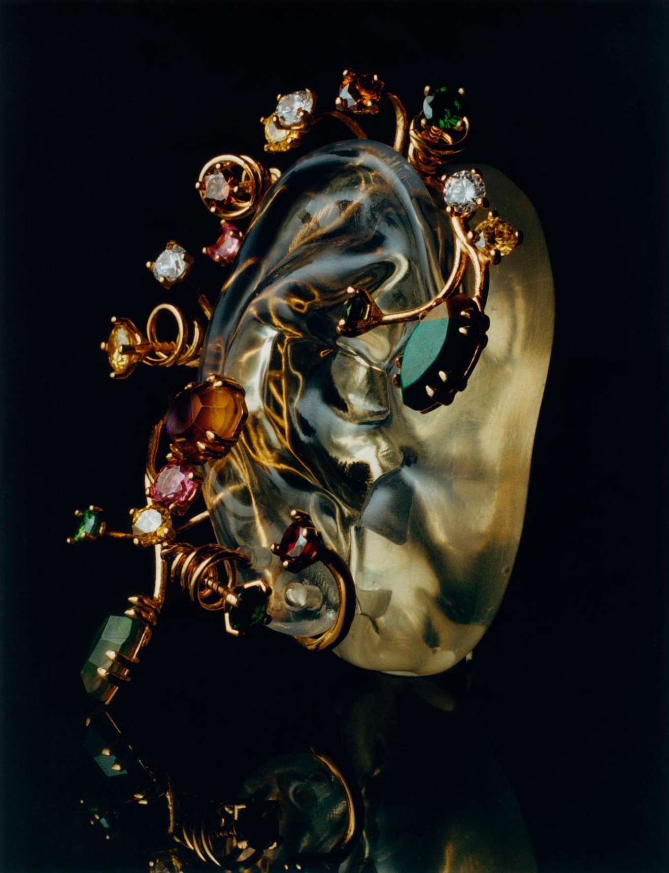 Translucent sculpture with embedded gemstones and gold wire accents on a reflective black surface, highlighting artistry and luxury.