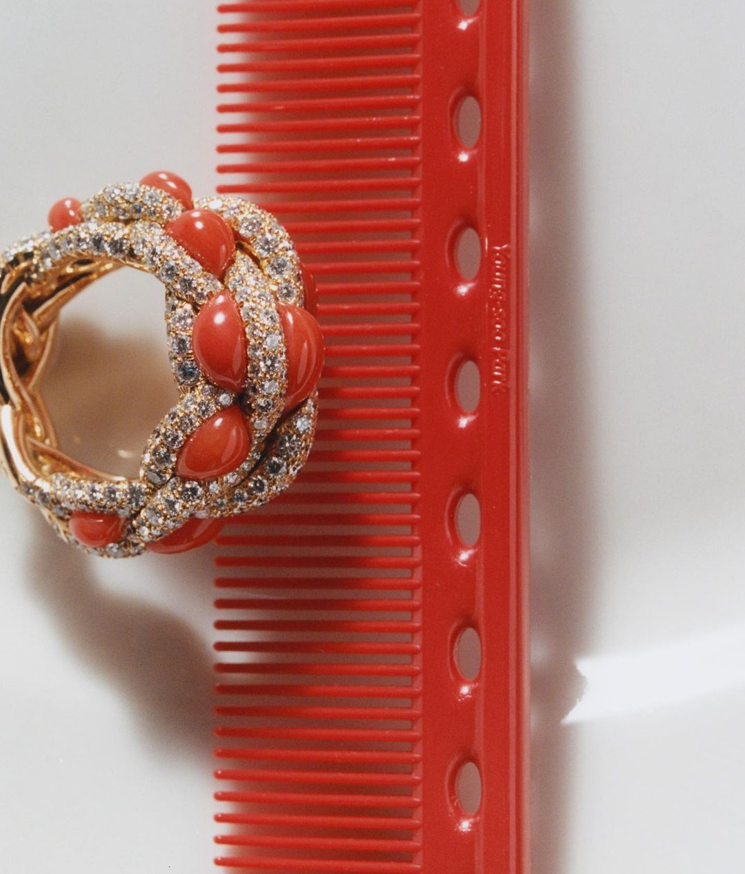 Gold ring with coral beads and diamond accents alongside a red plastic comb on a white surface, jewelry and beauty accessory.