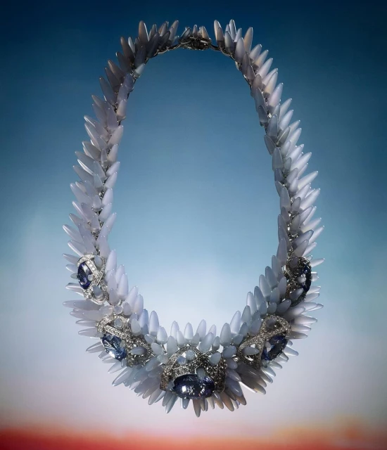 Elegant necklace featuring white spikes and blue gems on a graduated blue background. Jewelry design showcases unique spike and gem elements.