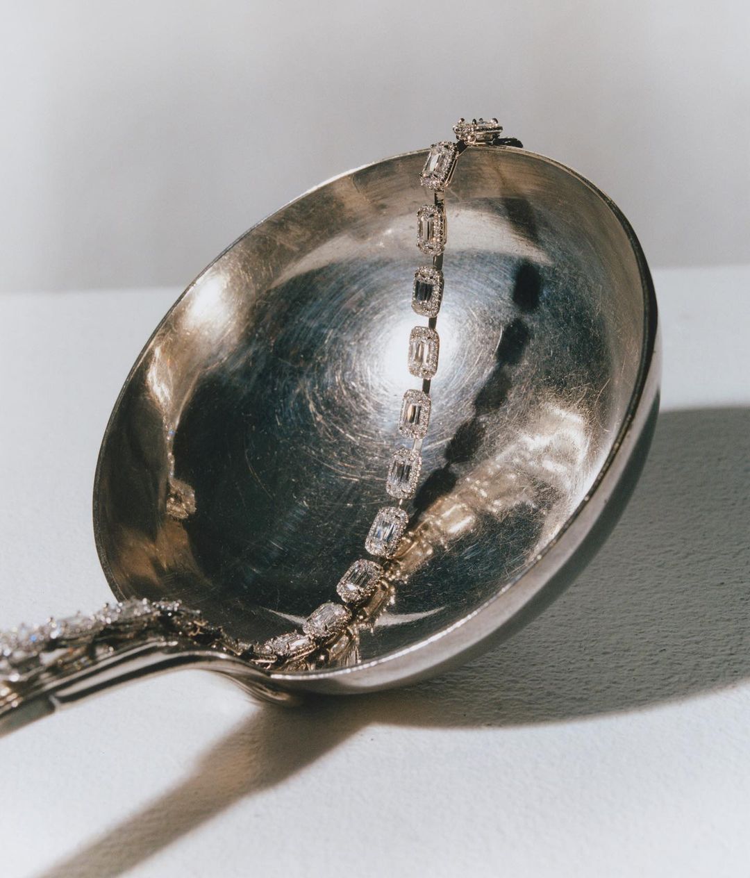 Diamond tennis bracelet on silver ladle with glossy surface. Studio photography highlighting luxury jewelry.