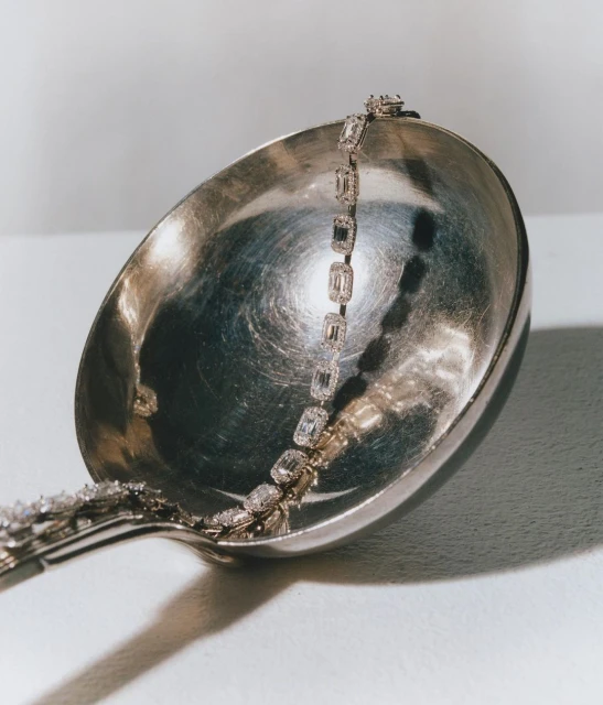 Diamond tennis bracelet on silver ladle with glossy surface. Studio photography highlighting luxury jewelry.