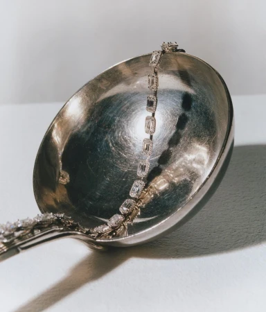 Diamond tennis bracelet on silver ladle with glossy surface. Studio photography highlighting luxury jewelry.