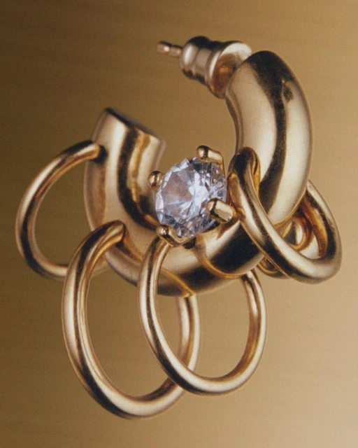 Close-up studio shot of a gold metal earring with a diamond set against a warm golden background. Fashion jewelry product shot.