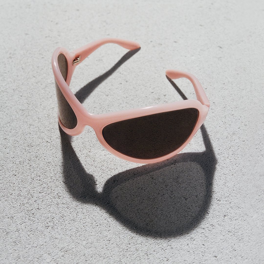 Stylish pink sunglasses with dark lenses casting a shadow on a textured light gray surface, fashion eyewear accessory for sun protection.