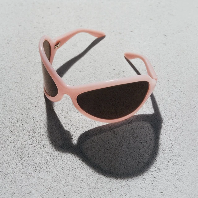 Stylish pink sunglasses with dark lenses casting a shadow on a textured light gray surface, fashion eyewear accessory for sun protection.
