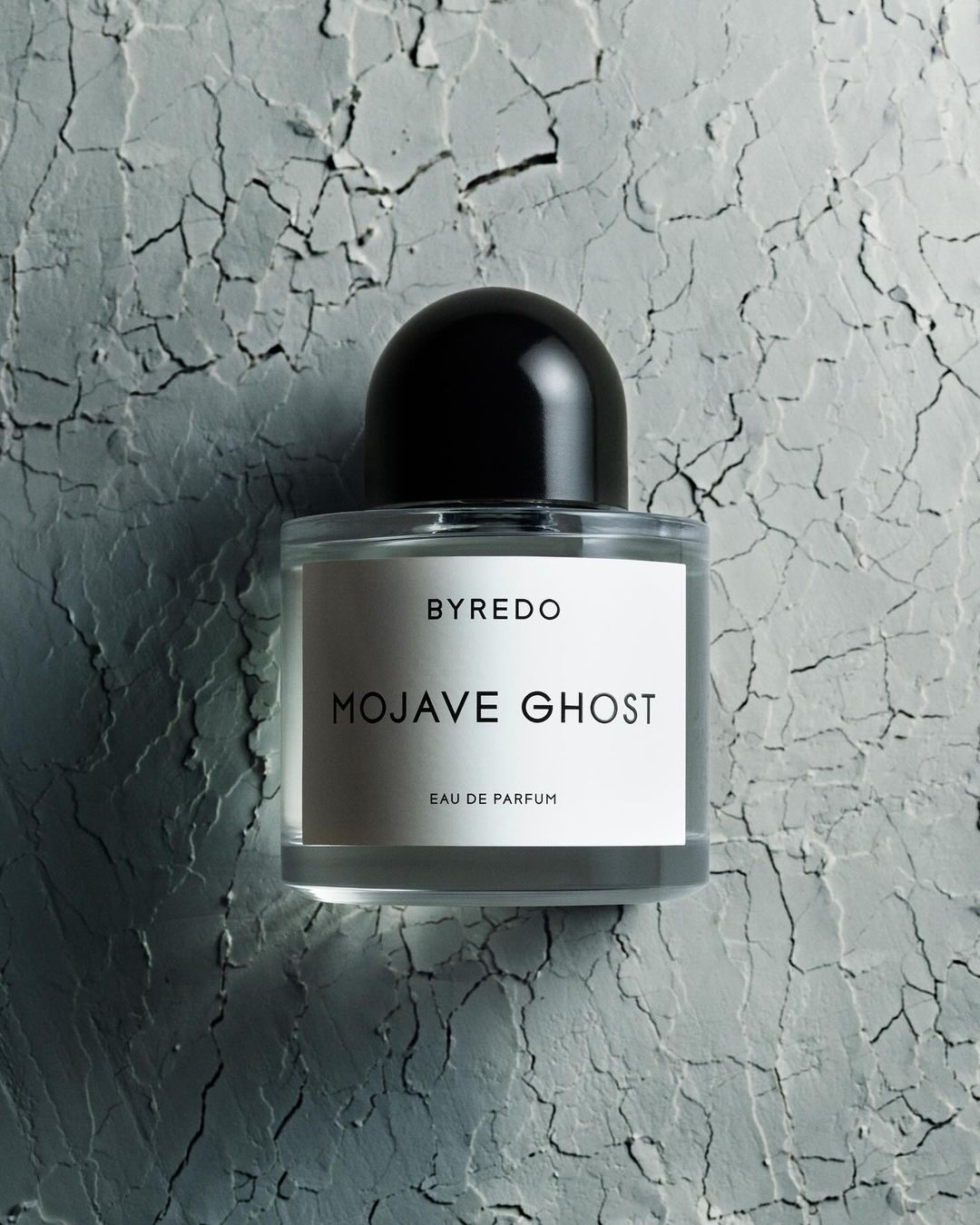 Byredo Mojave Ghost eau de parfum bottle on textured gray surface. Product shot of fragrance with sleek design and minimal label.