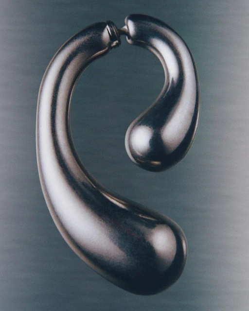 Abstract metal sculpture featuring smooth, curved forms, illuminated by soft, diffused light, set against a blurred grey background.