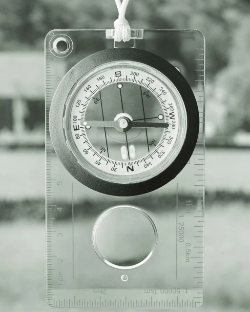 Overhead shot of a compass against a blurred background, showing direction, needle, and cardinal points with a clear casing and lanyard.