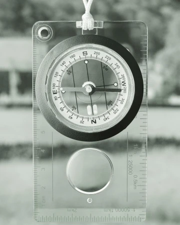 Overhead shot of a compass against a blurred background, showing direction, needle, and cardinal points with a clear casing and lanyard.