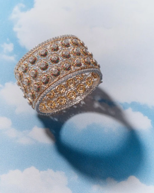 Gold and diamond cuff bracelet with intricate designs, set against a cloud-patterned backdrop in a soft, diffused studio light.