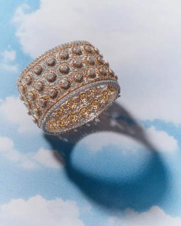 Gold and diamond cuff bracelet with intricate designs, set against a cloud-patterned backdrop in a soft, diffused studio light.