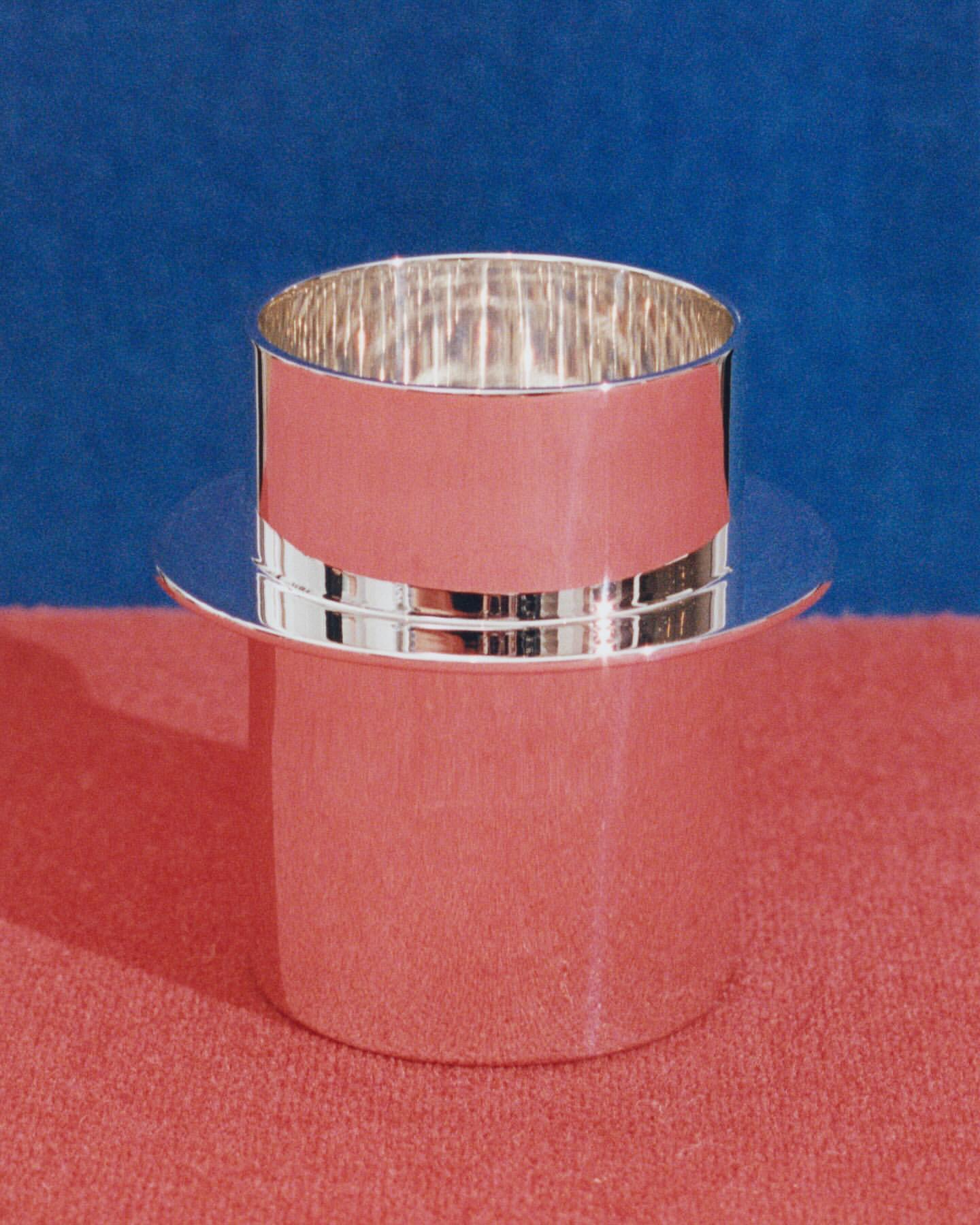 Silver-colored, hat-shaped container against a blue and pink background. The container is cylindrical with a wide, flat brim.