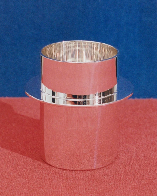 Silver-colored, hat-shaped container against a blue and pink background. The container is cylindrical with a wide, flat brim.
