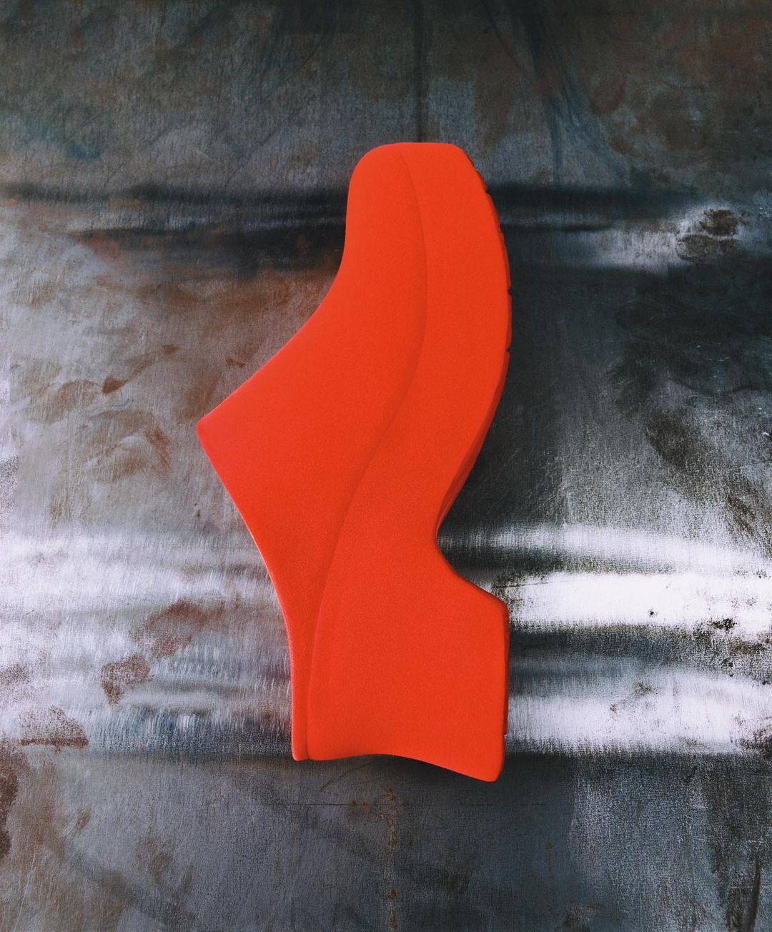 Abstract orange sculpture against a textured gray surface. Modern art with clean lines and a smooth finish, minimalist composition.