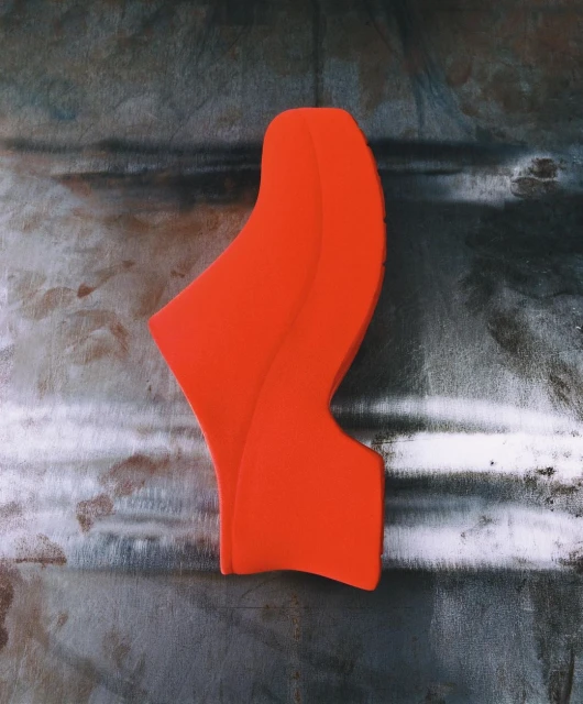 Abstract orange sculpture against a textured gray surface. Modern art with clean lines and a smooth finish, minimalist composition.