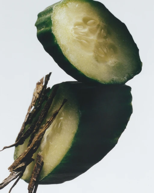 Close-up studio shot of a sliced cucumber on a reflective surface, showcasing its light green flesh, seeds, and dark green skin.
