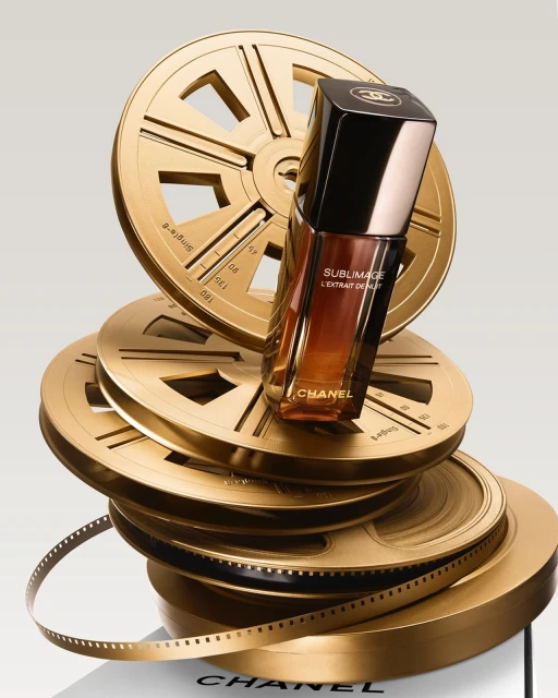 Chanel Sublimage L'extrait de Nuit serum rests on a stack of golden film reels, creating a luxurious beauty product still life.