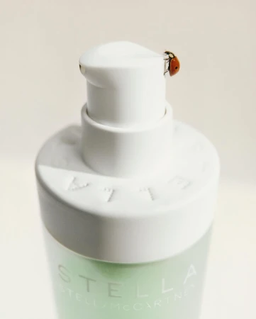 Close-up of a white pump bottle with a ladybug perched on top, softly lit against a neutral background, emphasizing the bottle's clean design.
