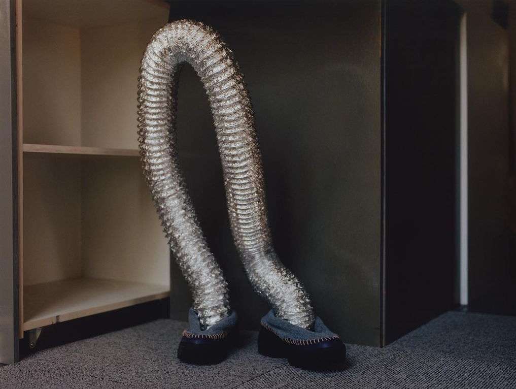 A silver flexible duct with shoes bends and appears to walk inside an empty shelving unit against a neutral backdrop.