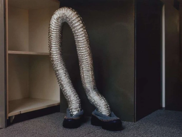 A silver flexible duct with shoes bends and appears to walk inside an empty shelving unit against a neutral backdrop.
