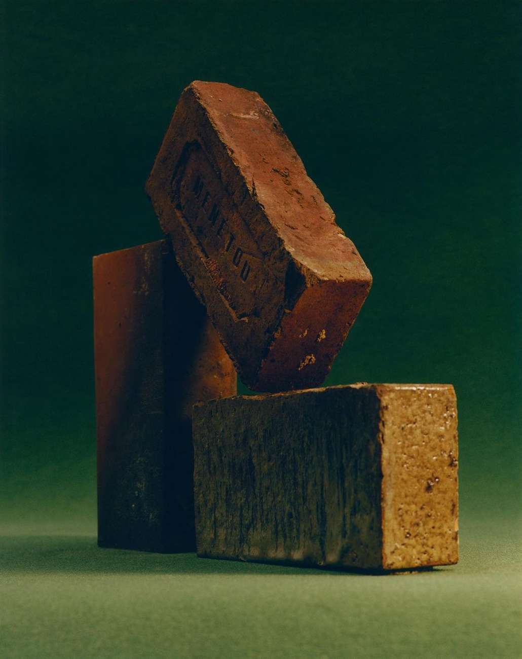 Three red bricks are stacked against a dark green background in a studio-lit, eye-level still life composition.
