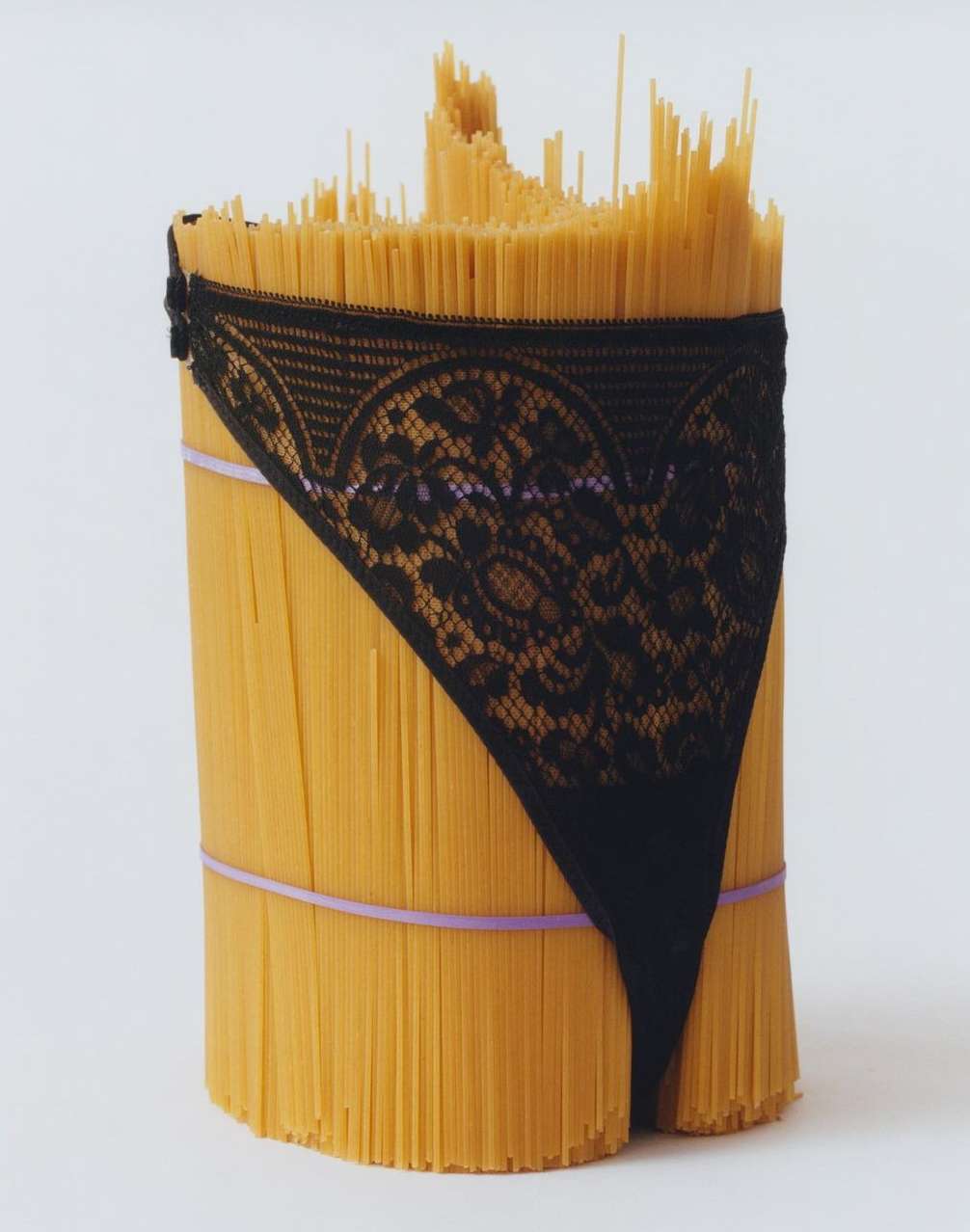Stylized still life of a pasta bundle wrapped with black lace lingerie and secured with bands on a white background, creative and unique.