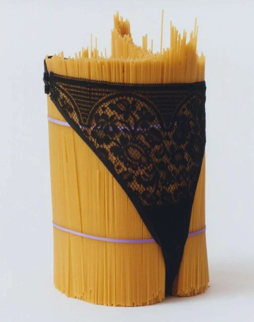 Stylized still life of a pasta bundle wrapped with black lace lingerie and secured with bands on a white background, creative and unique.