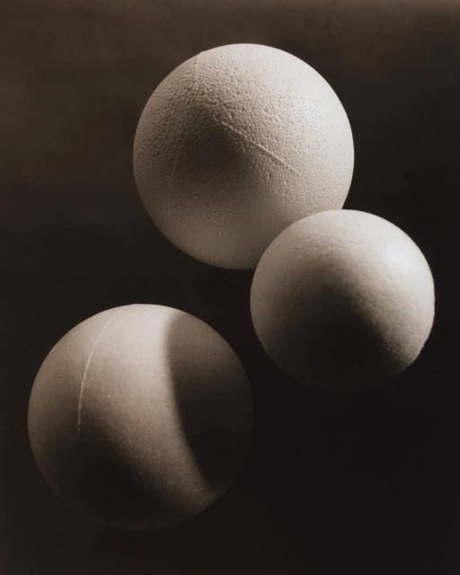 Still life photograph of three spherical objects with textured surfaces against a dark, neutral background in a studio setting.