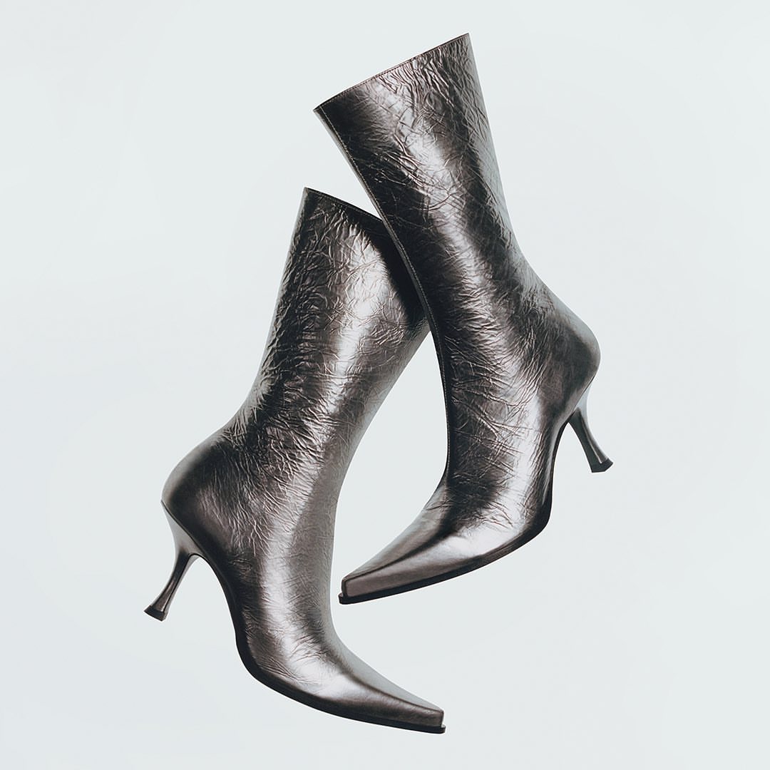 Pair of metallic silver heeled mid-calf boots isolated on a white background in a studio setting for a fashion advertisement.