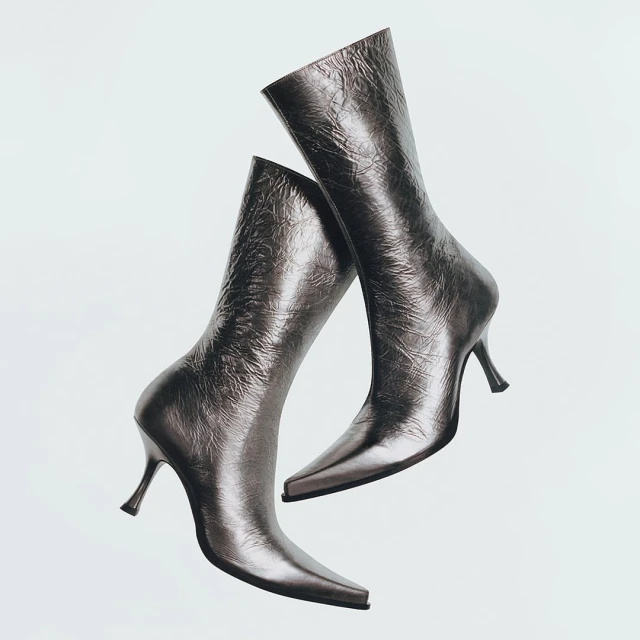 Pair of metallic silver heeled mid-calf boots isolated on a white background in a studio setting for a fashion advertisement.