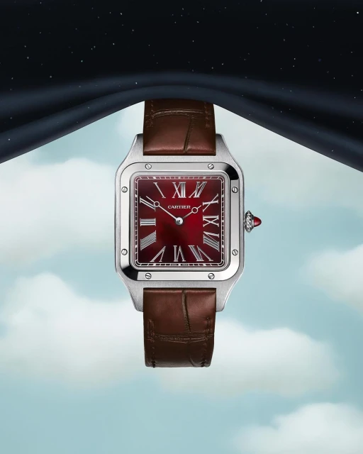 Luxury silver Cartier Santos watch with a red face and brown leather strap against a dreamy blue and black cloudy sky background.