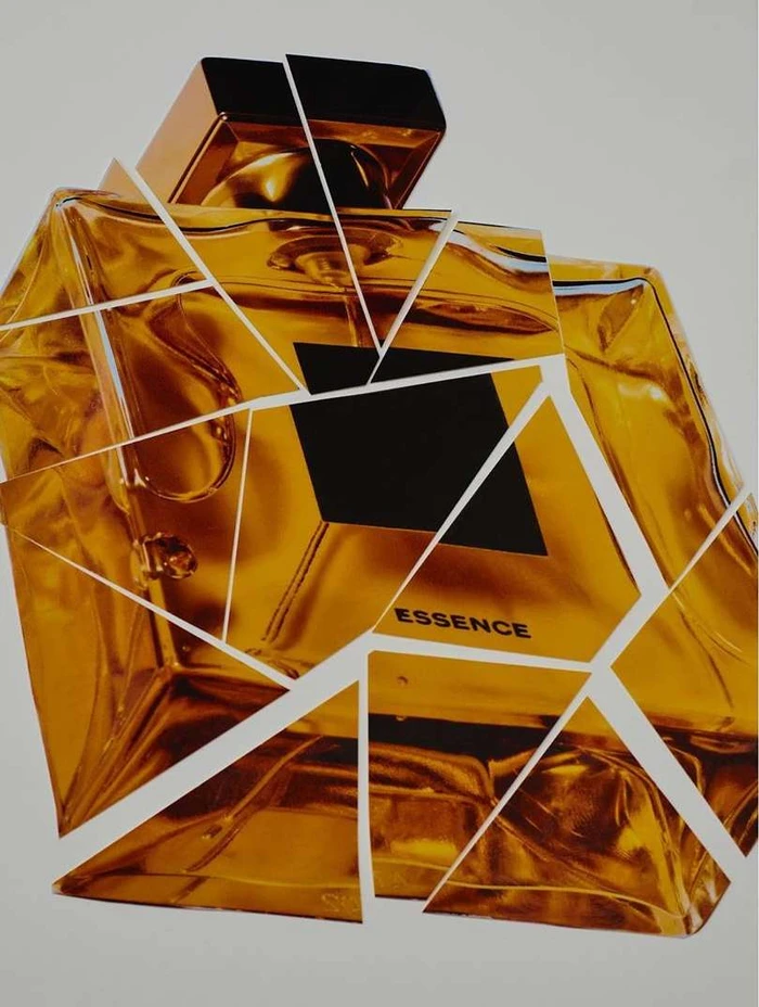 A shattered golden perfume bottle graphic composition with visible white fracture lines against a plain white background