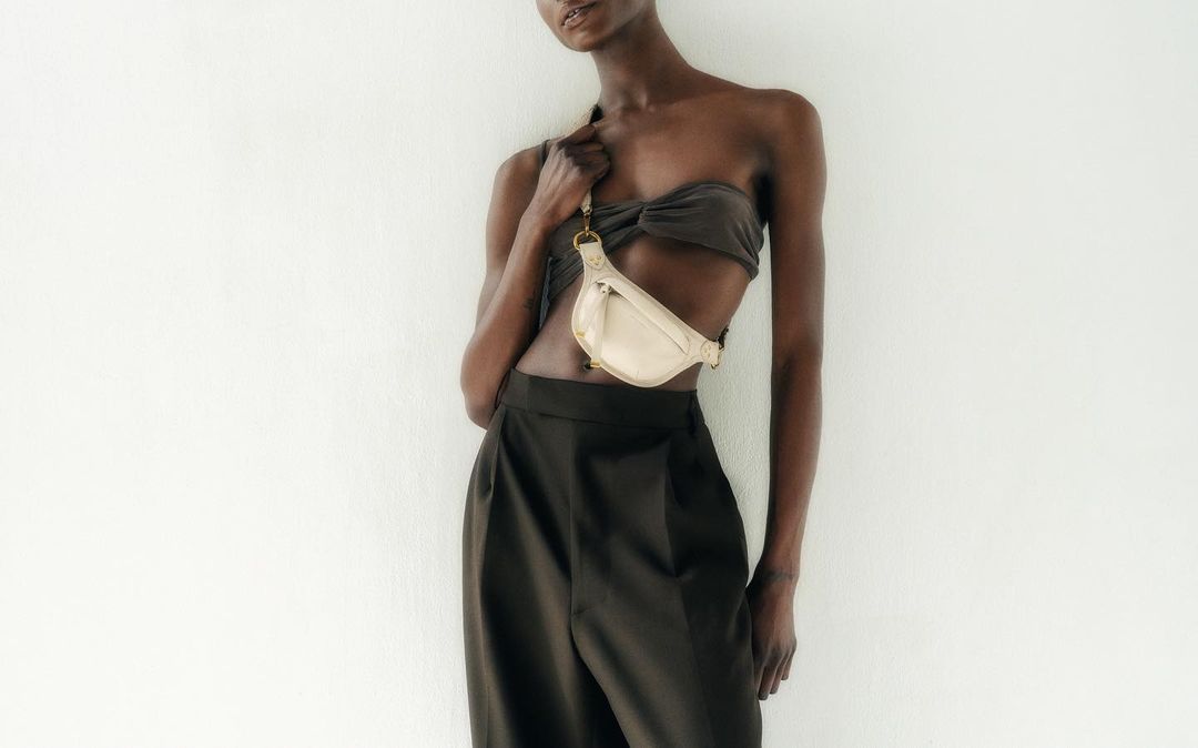 Studio shot of an African American adult female model wearing a tube top and trousers, posing against a white background with a purse.