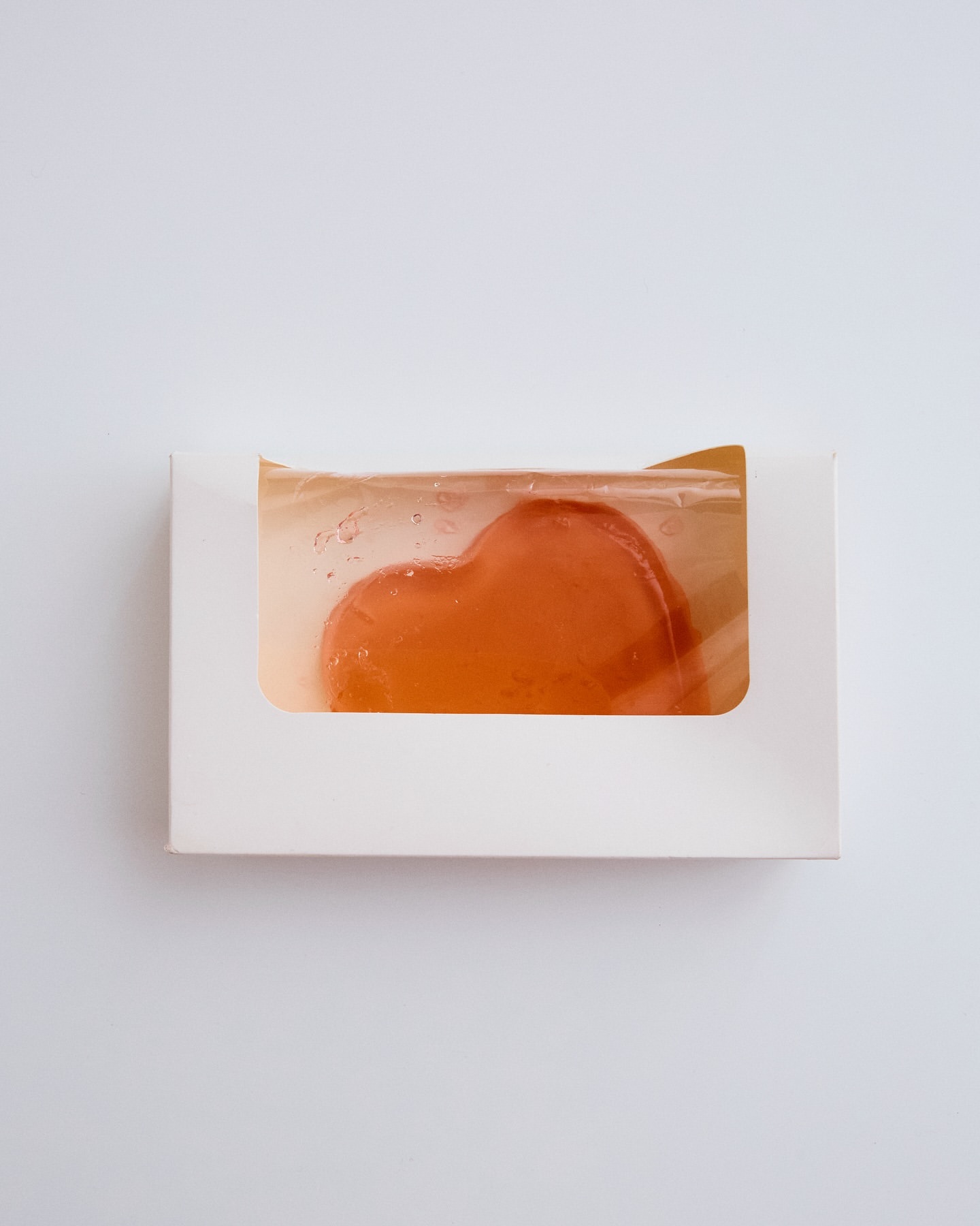 Heart-shaped soap bar inside a white box on a plain white background. The soap is translucent, and the box has a window to display the product.