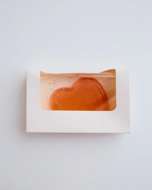 Heart-shaped soap bar inside a white box on a plain white background. The soap is translucent, and the box has a window to display the product.