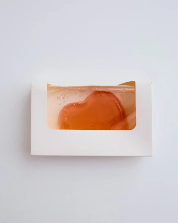 Heart-shaped soap bar inside a white box on a plain white background. The soap is translucent, and the box has a window to display the product.